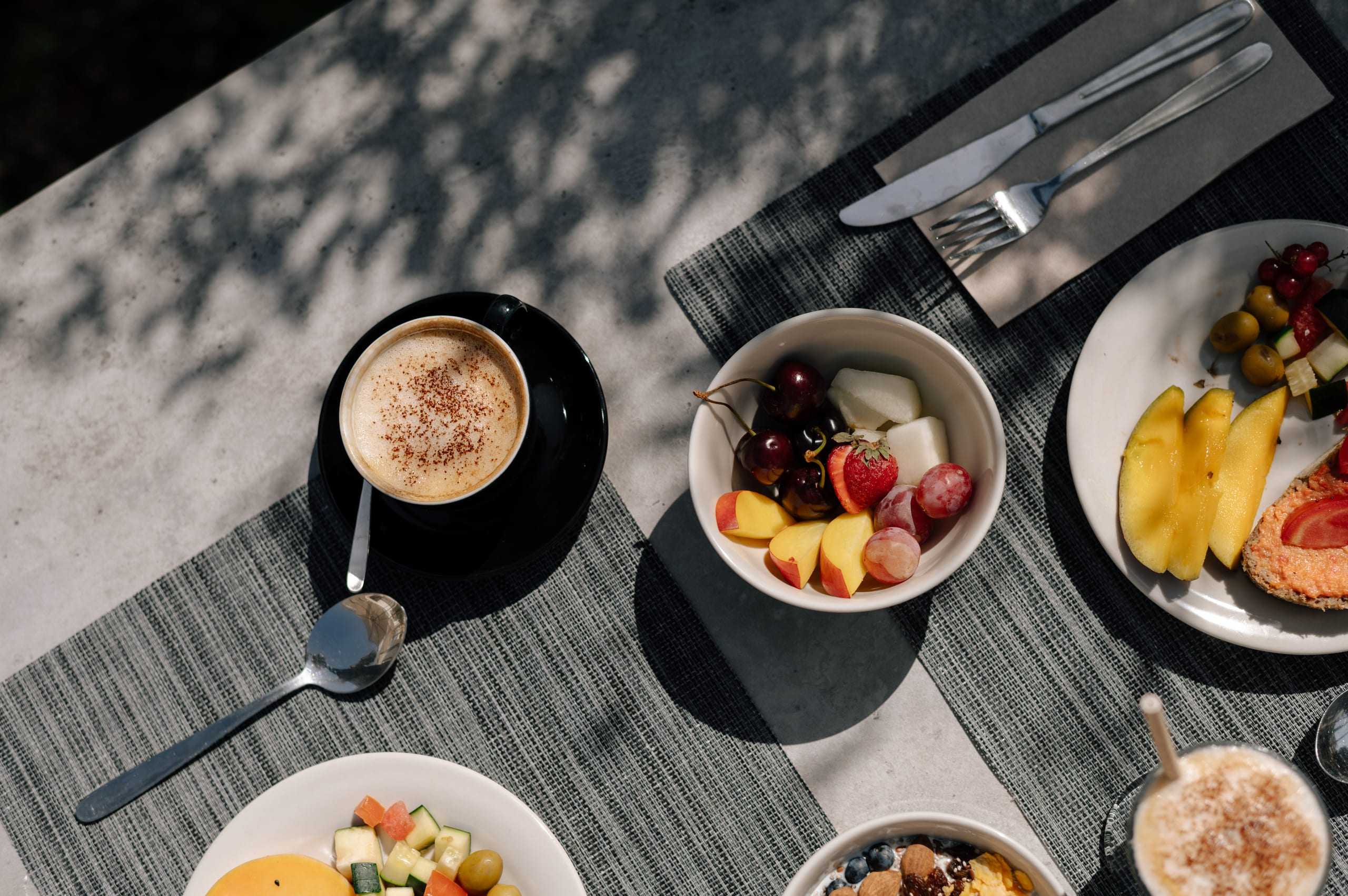 Frühstückstisch in der Sonne: Kaffee, Obst und Bowls